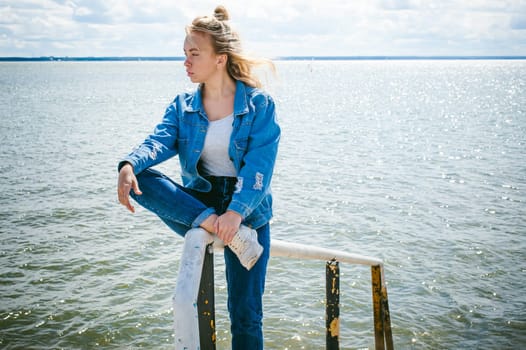young beautiful woman in jeans clothes outdoors. portrait of a girl with freckles on her face, stylish girl on sea beach, on a sunny summer autumn day.