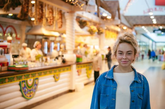 young beautiful woman in jeans clothes in business space of shopping center. portrait of a girl with freckles on her face, stylish girl standing near show-windows of fair in shopping center