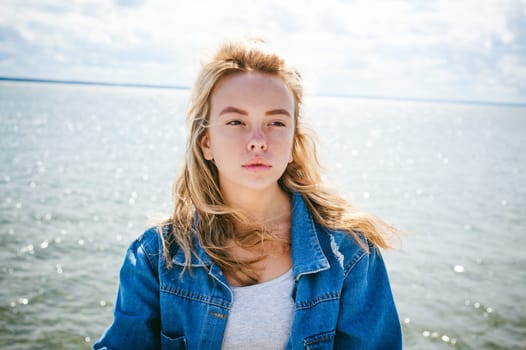 young beautiful woman in jeans clothes outdoors. portrait of a girl with freckles on her face, stylish girl on sea beach, on a sunny summer autumn day.