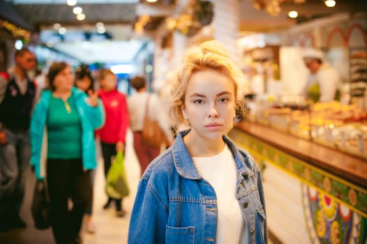 young beautiful woman in jeans clothes in business space of shopping center. portrait of a girl with freckles on her face, stylish girl standing near show-windows of fair in shopping center