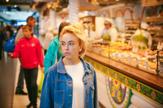 young beautiful woman in jeans clothes in business space of shopping center. portrait of a girl with freckles on her face, stylish girl standing near show-windows of fair in shopping center