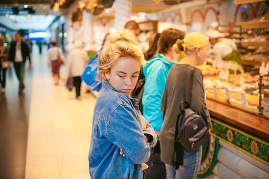 young beautiful woman in jeans clothes in business space of shopping center. portrait of a girl with freckles on her face, stylish girl standing near show-windows of fair in shopping center