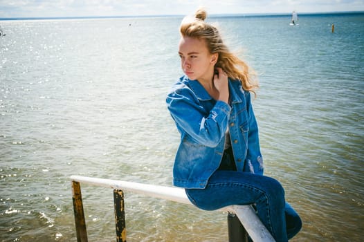 young beautiful woman in jeans clothes outdoors. portrait of a girl with freckles on her face, stylish girl on sea beach, on a sunny summer autumn day.