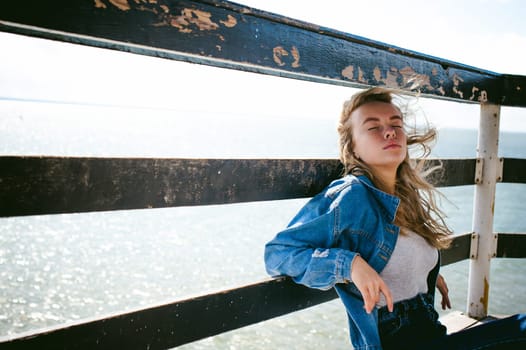 young beautiful woman in jeans clothes outdoors. portrait of a girl with freckles on her face, stylish girl on sea beach rescue tower, on a sunny summer autumn day.