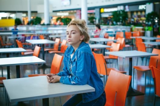 young beautiful woman in jeans clothes in business space of shopping center. portrait of a girl with freckles on her face, stylish girl in an empty cafe