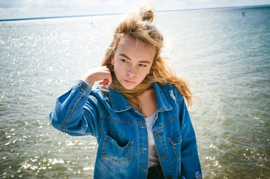young beautiful woman in jeans clothes outdoors. portrait of a girl with freckles on her face, stylish girl on sea beach, on a sunny summer autumn day.