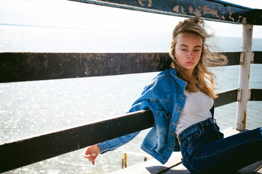 young beautiful woman in jeans clothes outdoors. portrait of a girl with freckles on her face, stylish girl on sea beach rescue tower, on a sunny summer autumn day.