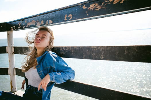 young beautiful woman in jeans clothes outdoors. portrait of a girl with freckles on her face, stylish girl on sea beach rescue tower, on a sunny summer autumn day.