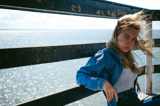 young beautiful woman in jeans clothes outdoors. portrait of a girl with freckles on her face, stylish girl on sea beach rescue tower, on a sunny summer autumn day.