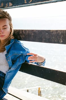 young beautiful woman in jeans clothes outdoors. portrait of a girl with freckles on her face, stylish girl on sea beach rescue tower, on a sunny summer autumn day.