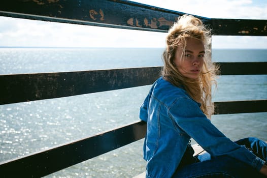 young beautiful woman in jeans clothes outdoors. portrait of a girl with freckles on her face, stylish girl on sea beach rescue tower, on a sunny summer autumn day.