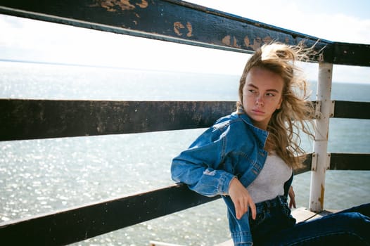 young beautiful woman in jeans clothes outdoors. portrait of a girl with freckles on her face, stylish girl on sea beach rescue tower, on a sunny summer autumn day.
