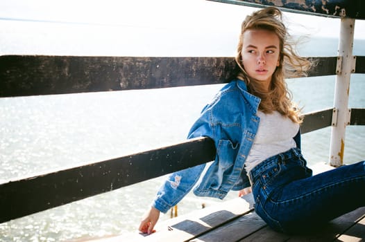 young beautiful woman in jeans clothes outdoors. portrait of a girl with freckles on her face, stylish girl on sea beach rescue tower, on a sunny summer autumn day.