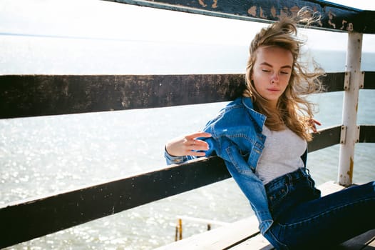 young beautiful woman in jeans clothes outdoors. portrait of a girl with freckles on her face, stylish girl on sea beach rescue tower, on a sunny summer autumn day.