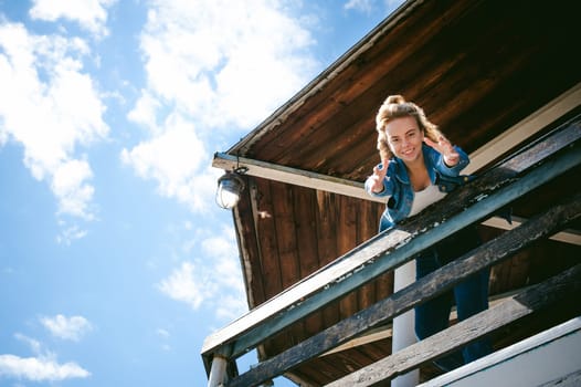 young beautiful woman in jeans clothes outdoors. portrait of a girl with freckles on her face, stylish girl on sea beach rescue tower, on a sunny summer autumn day. happy pulls hands to hug