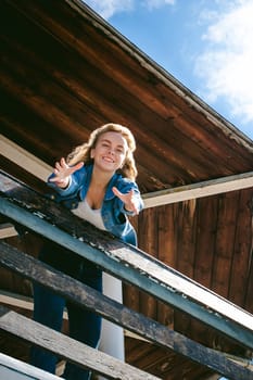 young beautiful woman in jeans clothes outdoors. portrait of a girl with freckles on her face, stylish girl on sea beach rescue tower, on a sunny summer autumn day. happy pulls hands to hug