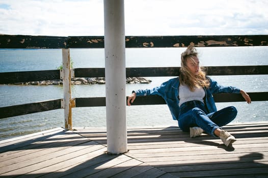 young beautiful woman in jeans clothes outdoors. portrait of a girl with freckles on her face, stylish girl on sea beach rescue tower, on a sunny summer autumn day.
