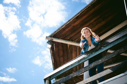 young beautiful woman in jeans clothes outdoors. portrait of a girl with freckles on her face, stylish girl on sea beach rescue tower, on a sunny summer autumn day. happy pulls hands to hug