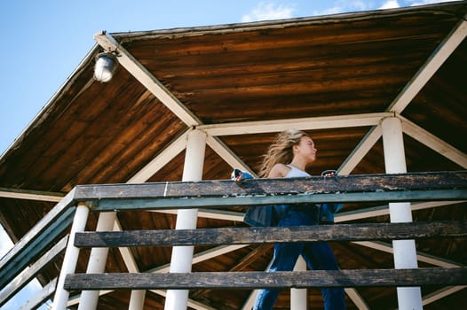 young beautiful woman in jeans clothes outdoors. portrait of a girl with freckles on her face, stylish girl on sea beach rescue tower, on a sunny summer autumn day.