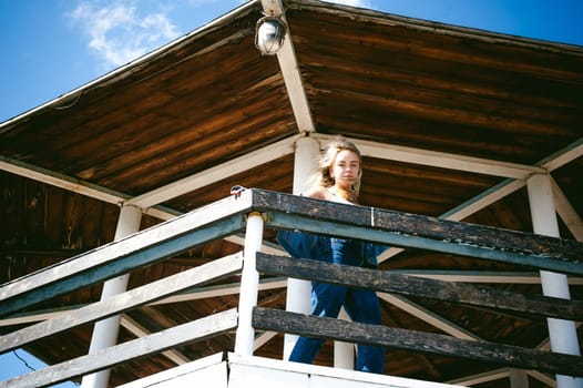 young beautiful woman in jeans clothes outdoors. portrait of a girl with freckles on her face, stylish girl on sea beach rescue tower, on a sunny summer autumn day.
