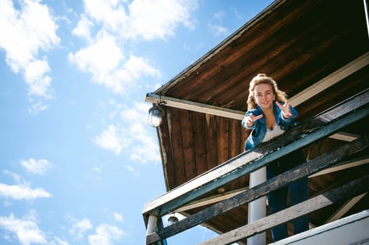 young beautiful woman in jeans clothes outdoors. portrait of a girl with freckles on her face, stylish girl on sea beach rescue tower, on a sunny summer autumn day. happy pulls hands to hug