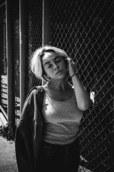 young woman in jeans clothes outdoors. portrait of a girl with freckles on her face, stylish girl on a fence of a grid, a sunny summer day...
