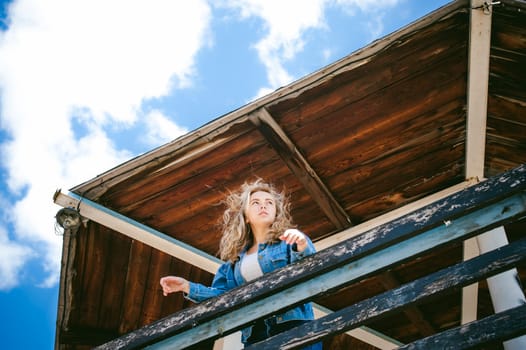 young beautiful woman in jeans clothes outdoors. portrait of a girl with freckles on her face, stylish girl on sea beach rescue tower, on a sunny summer autumn day.