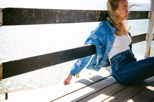 young beautiful woman in jeans clothes outdoors. portrait of a girl with freckles on her face, stylish girl on sea beach rescue tower, on a sunny summer autumn day.