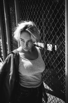 young woman in jeans clothes outdoors. portrait of a girl with freckles on her face, stylish girl on a fence of a grid, a sunny summer day...