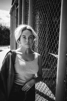young woman in jeans clothes outdoors. portrait of a girl with freckles on her face, stylish girl on a fence of a grid, a sunny summer day...