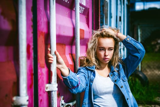 young beautiful woman in jeans clothes outdoors. portrait of a girl with freckles on her face, stylish girl on a freight containers background, on a sunny summer day.