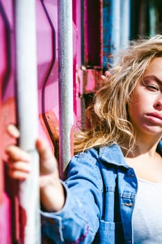 young beautiful woman in jeans clothes outdoors. portrait of a girl with freckles on her face, stylish girl on a freight containers background, on a sunny summer day.