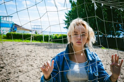 young woman in jeans clothes outdoors. portrait of a girl with freckles on her face, against the background of a football gate grid, on a sunny summer day