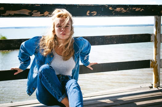young beautiful woman in jeans clothes outdoors. portrait of a girl with freckles on her face, stylish girl on sea beach rescue tower, on a sunny summer autumn day.