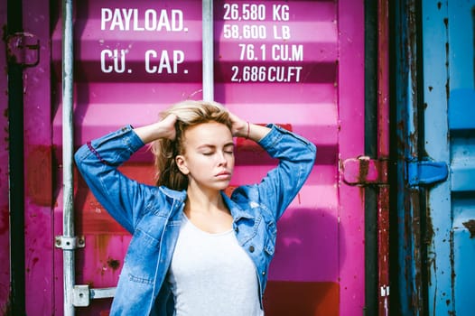 young beautiful woman in jeans clothes outdoors. portrait of a girl with freckles on her face, stylish girl on a freight containers background, on a sunny summer day.