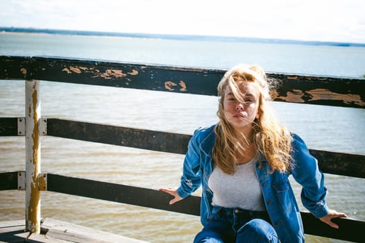 young beautiful woman in jeans clothes outdoors. portrait of a girl with freckles on her face, stylish girl on sea beach rescue tower, on a sunny summer autumn day.
