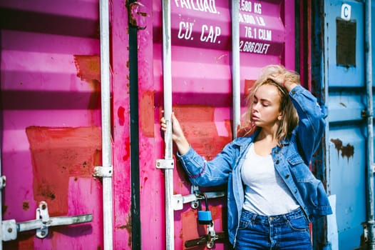 young beautiful woman in jeans clothes outdoors. portrait of a girl with freckles on her face, stylish girl on a freight containers background, on a sunny summer day.