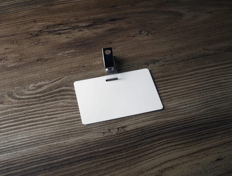 Blank badge mockup on wooden background. White plastic id card. Space for text.