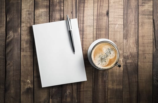 Blank book, pencil and coffee cup on wooden table background. Stationery elements. Template for placing your design.