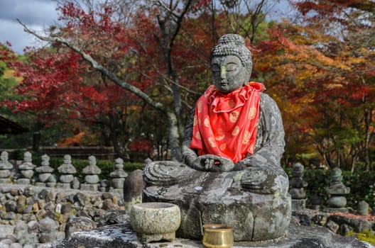 Stone statue of Buddha with autumn colored leaves in Adashino Nenbutsuji Temple, Kyoto, Japan