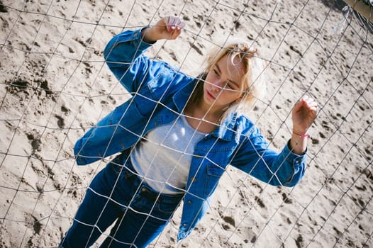 young woman in jeans clothes outdoors. portrait of a girl with freckles on her face, against the background of a football gate grid, on a sunny summer day