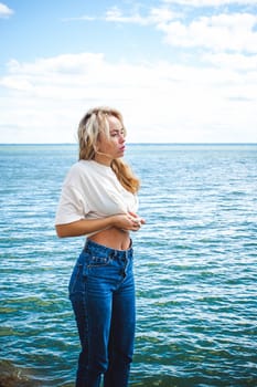 Portrait young woman on stones near sea. Beautiful girl is resting on coast, enjoying outdoor recreation.