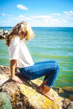 Portrait young woman on stones near sea. Beautiful girl is resting on coast, enjoying outdoor recreation.