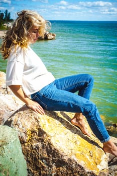 Portrait young woman on stones near sea. Beautiful girl is resting on coast, enjoying outdoor recreation.