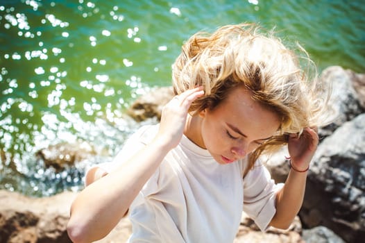 Portrait young woman on stones near sea. Beautiful girl is resting on coast, enjoying outdoor recreation.