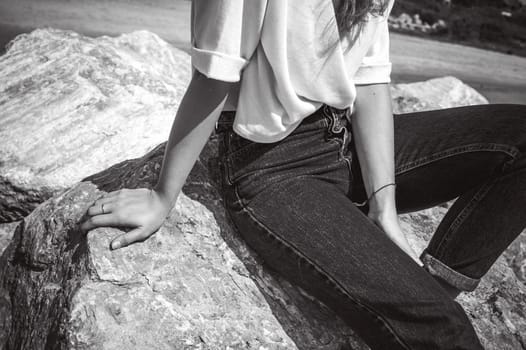Portrait young woman on stones near sea. Beautiful girl is resting on coast, enjoying outdoor recreation.