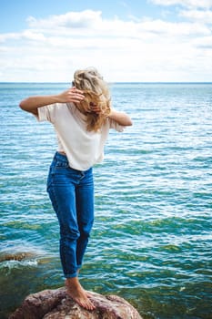 Portrait young woman on stones near sea. Beautiful girl is resting on coast, enjoying outdoor recreation.