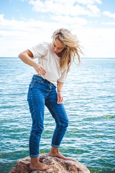 Portrait young woman on stones near sea. Beautiful girl is resting on coast, enjoying outdoor recreation.