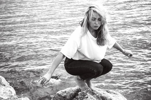 Portrait young woman on stones near sea. Beautiful girl is resting on coast, enjoying outdoor recreation.
