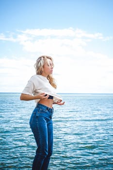 Portrait young woman on stones near sea. Beautiful girl is resting on coast, enjoying outdoor recreation.